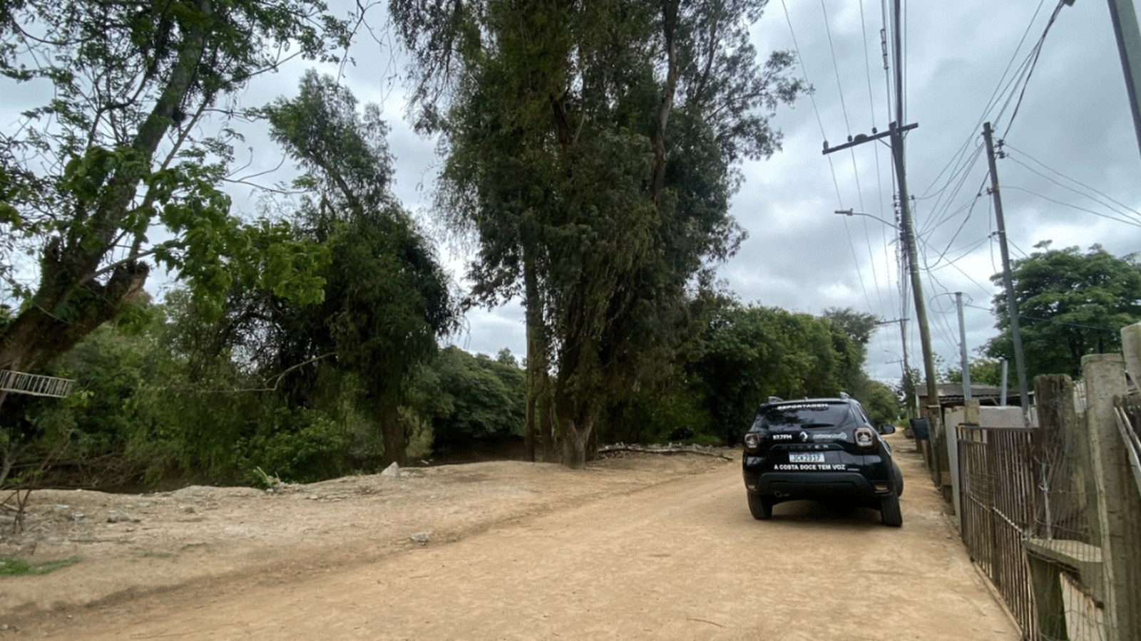 Galhos de árvore de grande porte pendurados sobre fiação elétrica em rua residencial de Camaquã